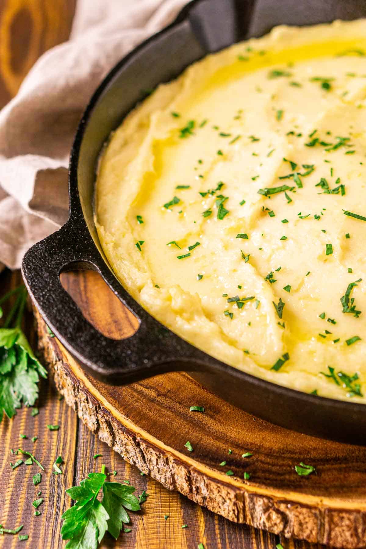 A black cast-iron skillet filled with the smoked mashed potatoes with chopped parsley to the left and a napkin in the background.