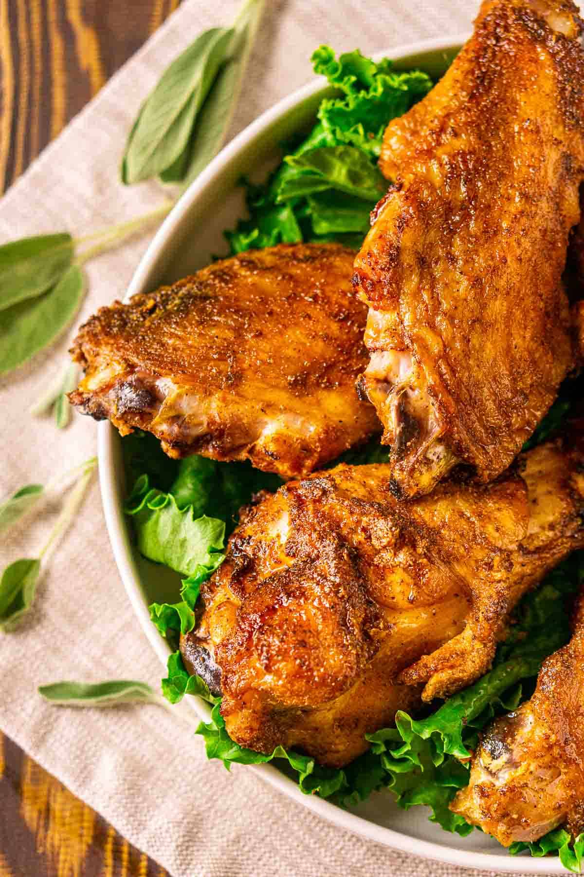 An aerial view of the smoked turkey wings on a white platter with green leaf lettuce and herbs to the side.