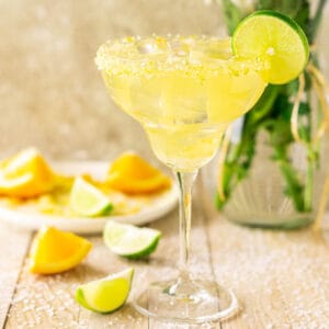A Texas margarita on a cream-colored wooden board with salt scattered around it and pieces of cut orange and lime.