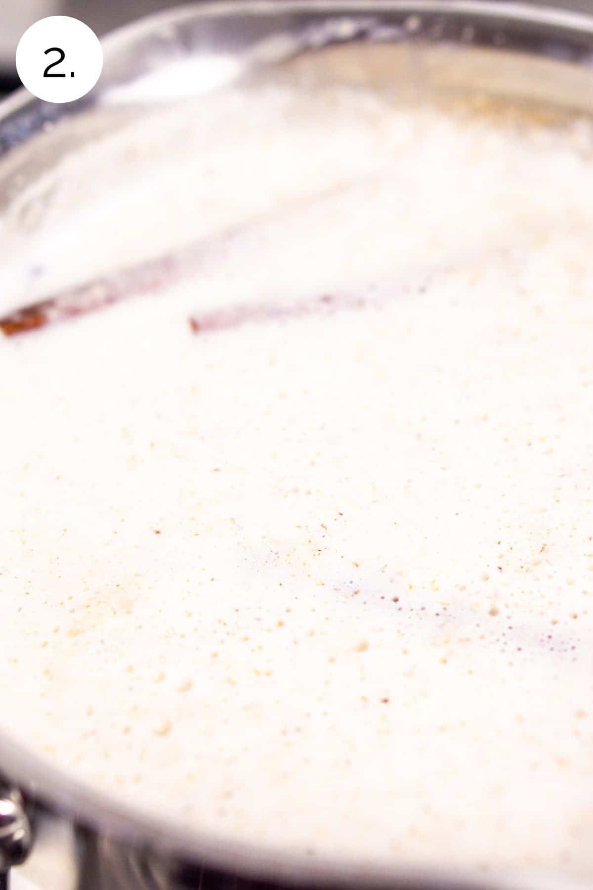The milk and cream mixture in a small saucepan with cinnamon sticks on the stove-top.