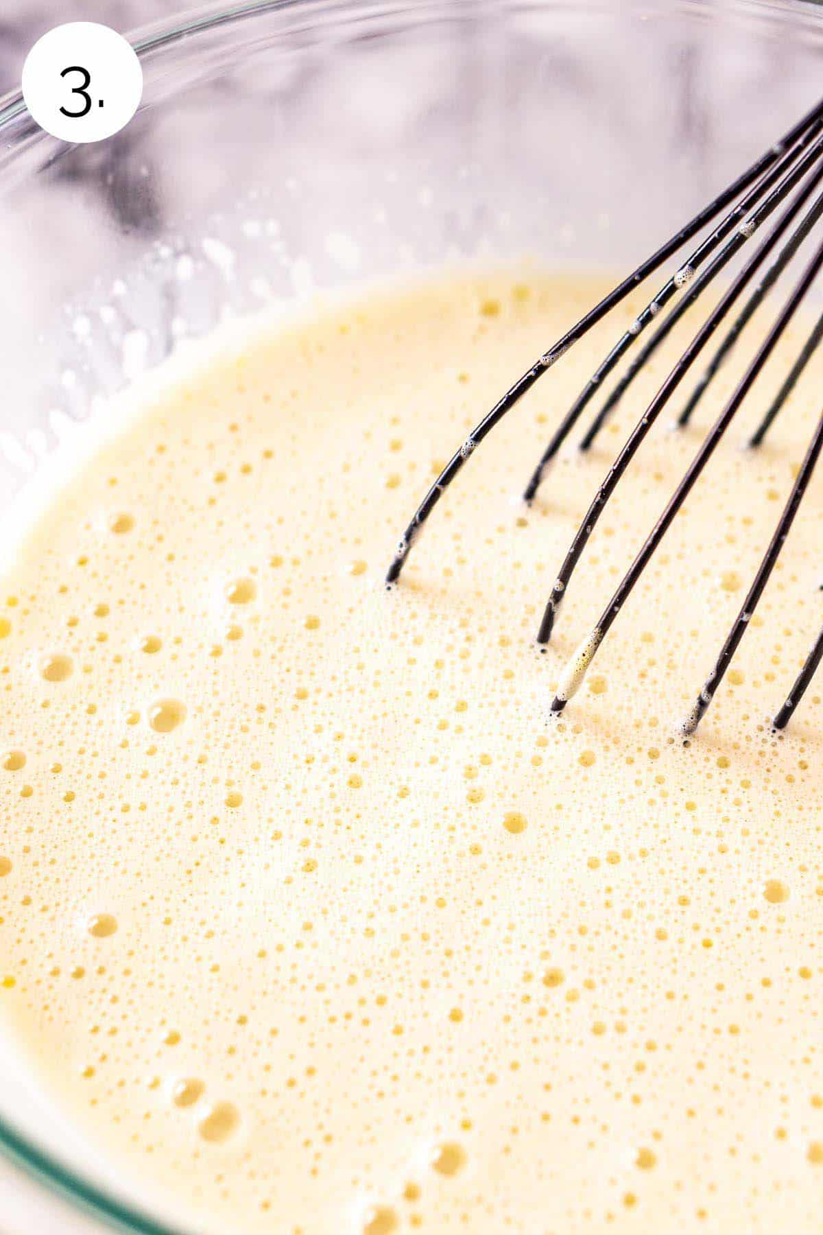 Whisking the egg yolks and cream mixture together in a large glass mixing bowl.