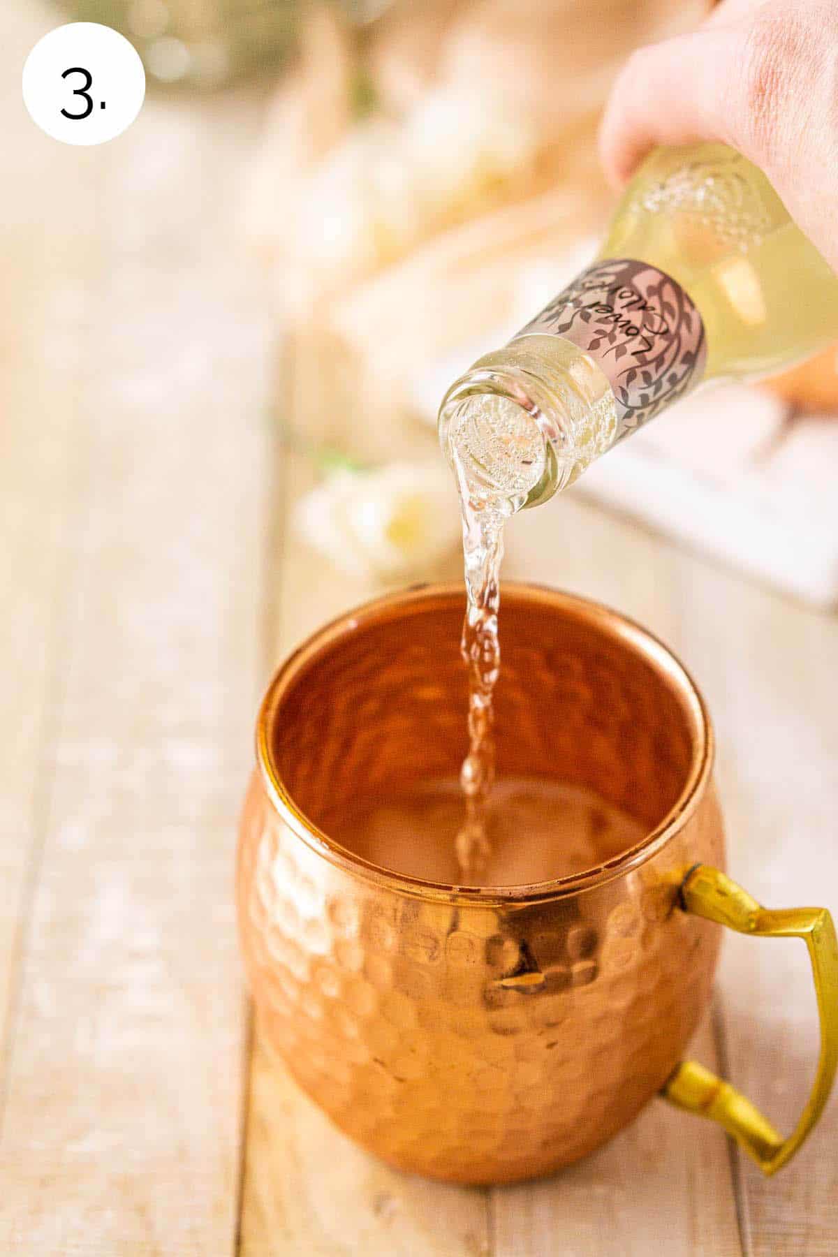 A hand pouring the chilled ginger beer into the copper mug with the other ingredients.
