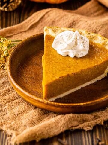 A close-up shot of the maple-bourbon pumpkin pie on a small wooden plate on top of a piece of cheese clothe.