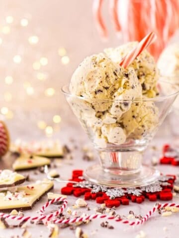 A glass dessert cup filled with the peppermint bark ice cream with chopped chocolate and a decorative ribbon around it and lights in the background.