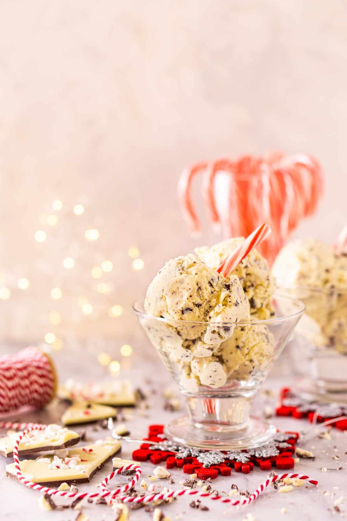 A glass dessert cup filled with the peppermint bark ice cream with chopped chocolate and a decorative ribbon around it and lights in the background.