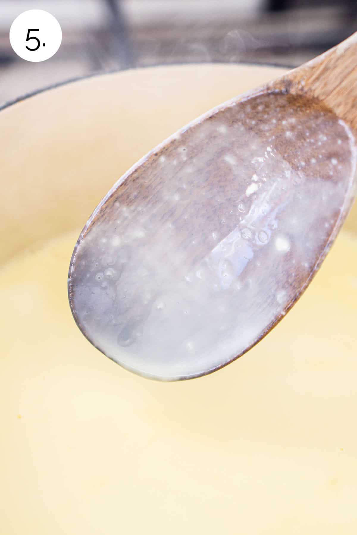 A wooden spoon over the cream mixture showing how it coats the surface well.