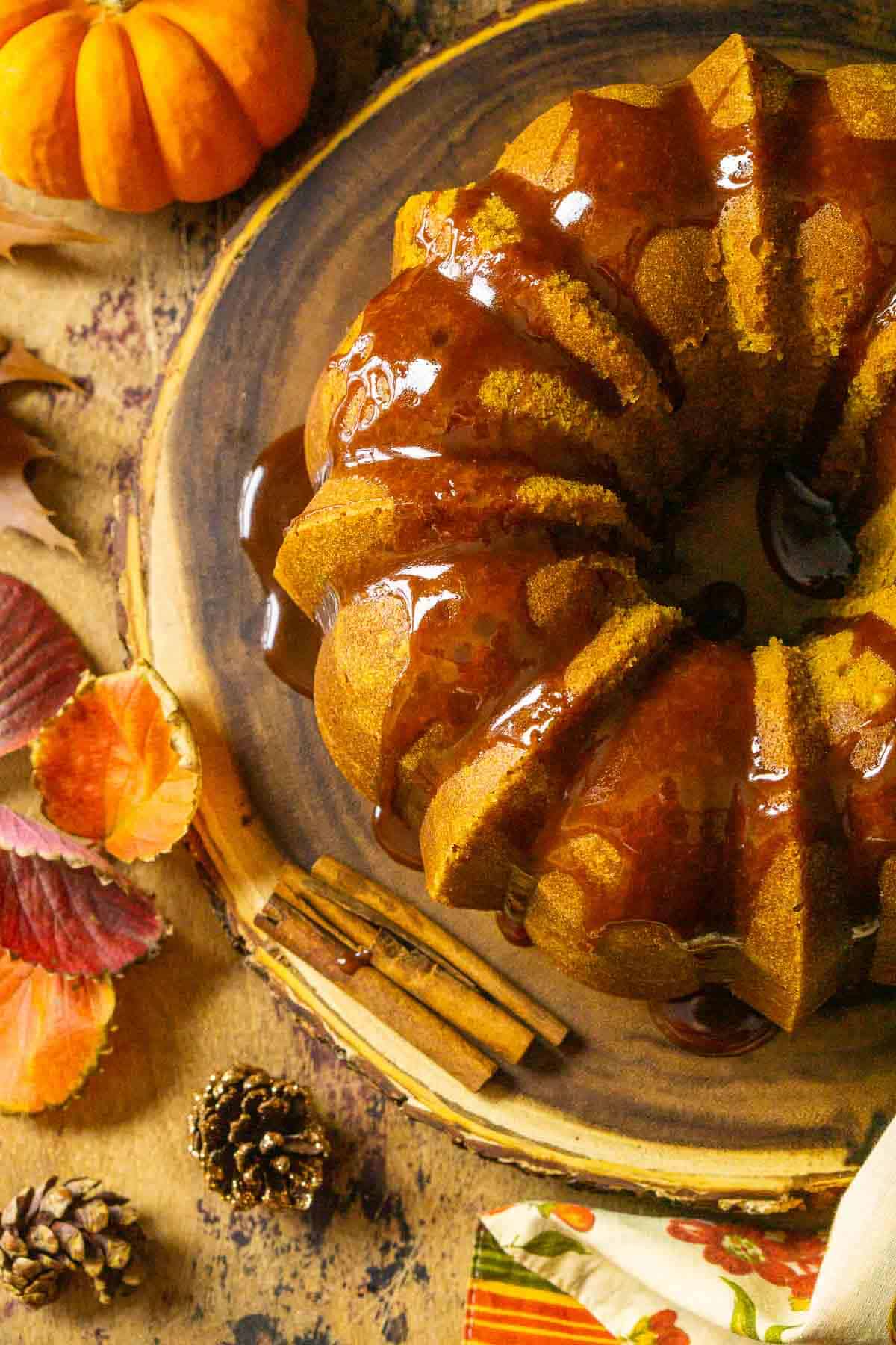 An aerial view of the pumpkin pound cake on a wooden platter with fall decor all around it on a wooden surface.