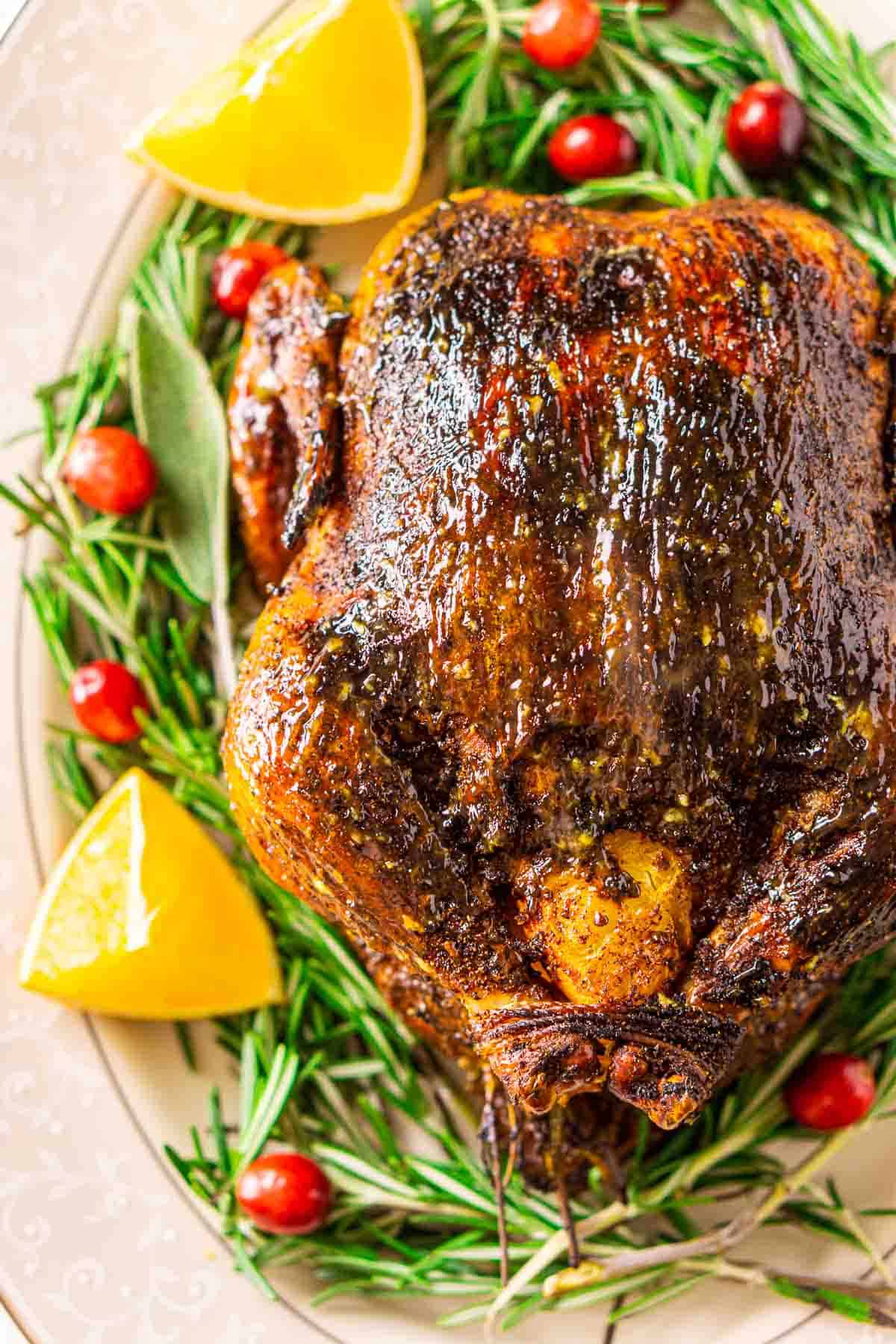 An aerial view of the roast Christmas chicken on a white serving platter with rosemary, cranberries and oranges surrounding it.