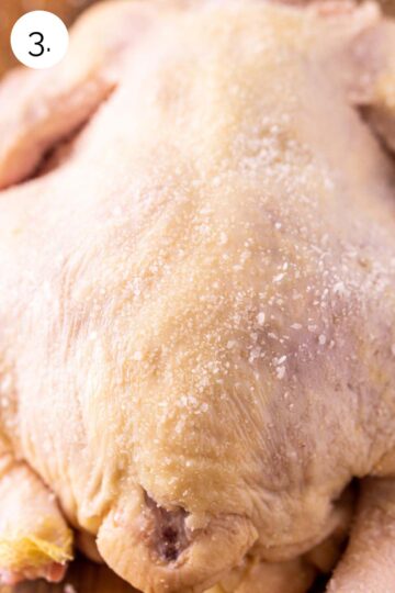 The chicken sprinkled with salt on a brown wooden cutting board before dry brining in the refrigerator.