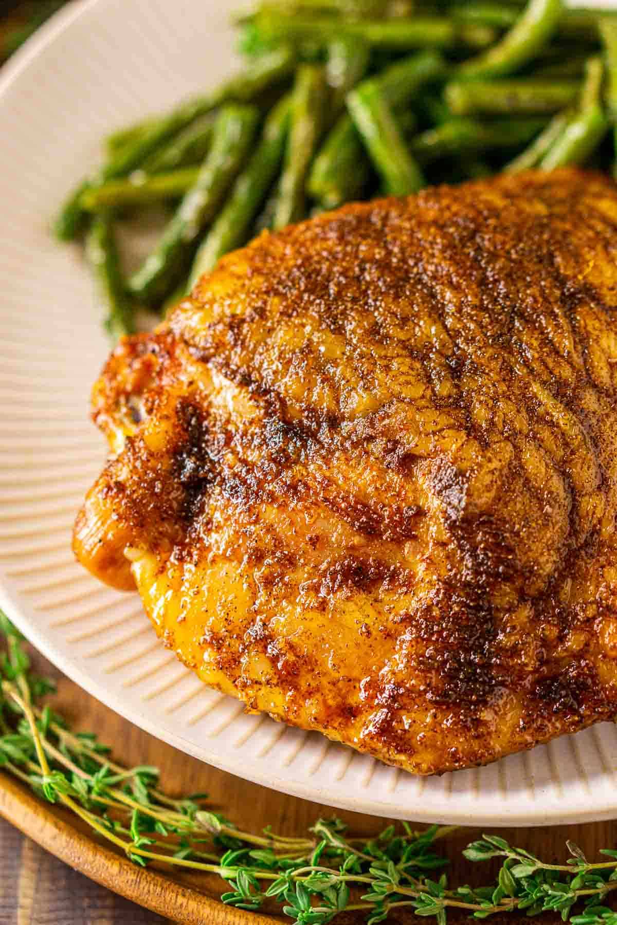 A close-up of the smoked turkey thighs on a white plate with several sprigs of fresh thyme in front.