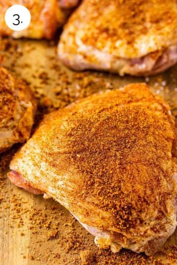 The turkey thighs on a brown wooden cutting board covered with the dry spice rub before cooking.