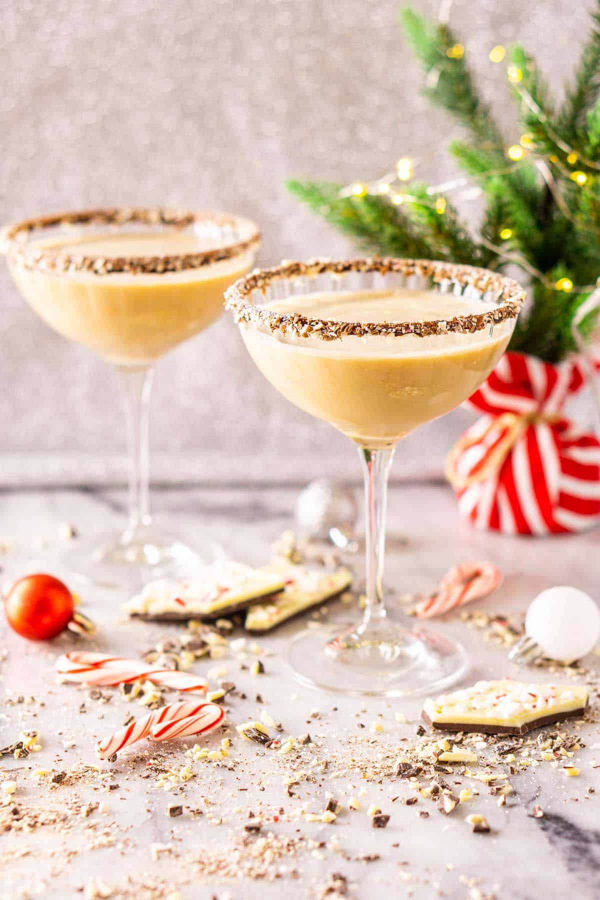 Two peppermint-chocolate martinis on a white marble countertop with grated peppermint bark all around them.