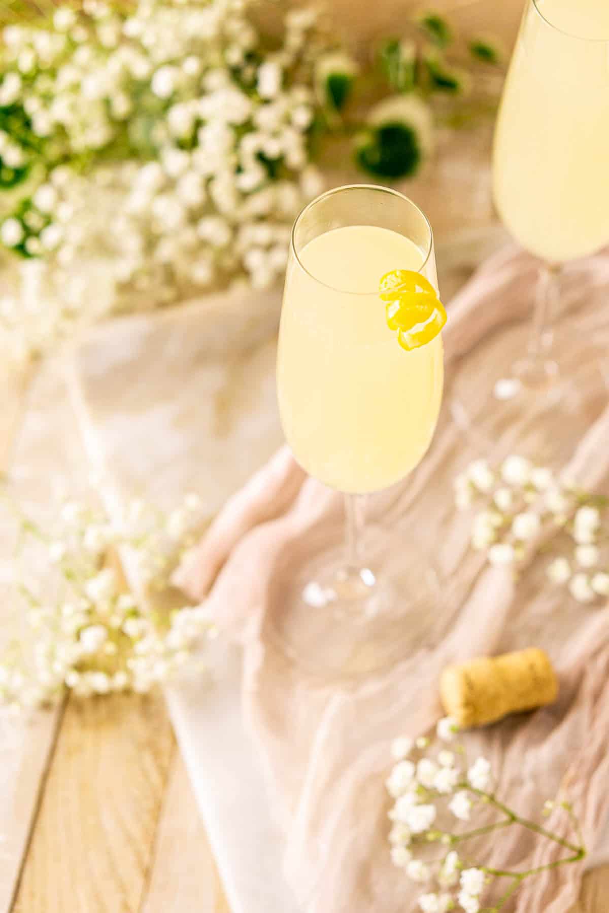 Looking down on a French 77 cocktail on a white marble board with white flowers surrounding it.
