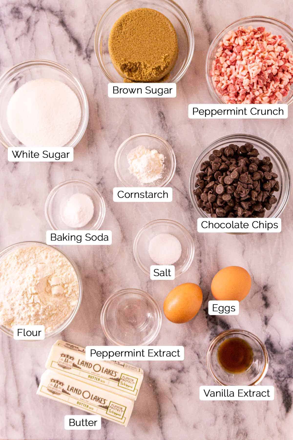 The cookie ingredients on a white marble countertop with white and black labels by every food item.