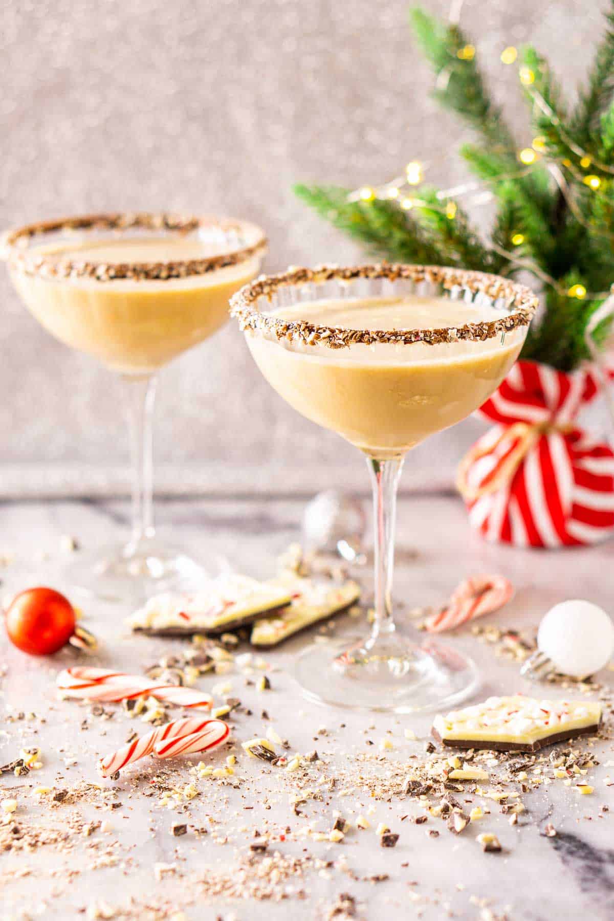 Two peppermint-chocolate martinis on a white marble countertop with crushed peppermint bark all around them.