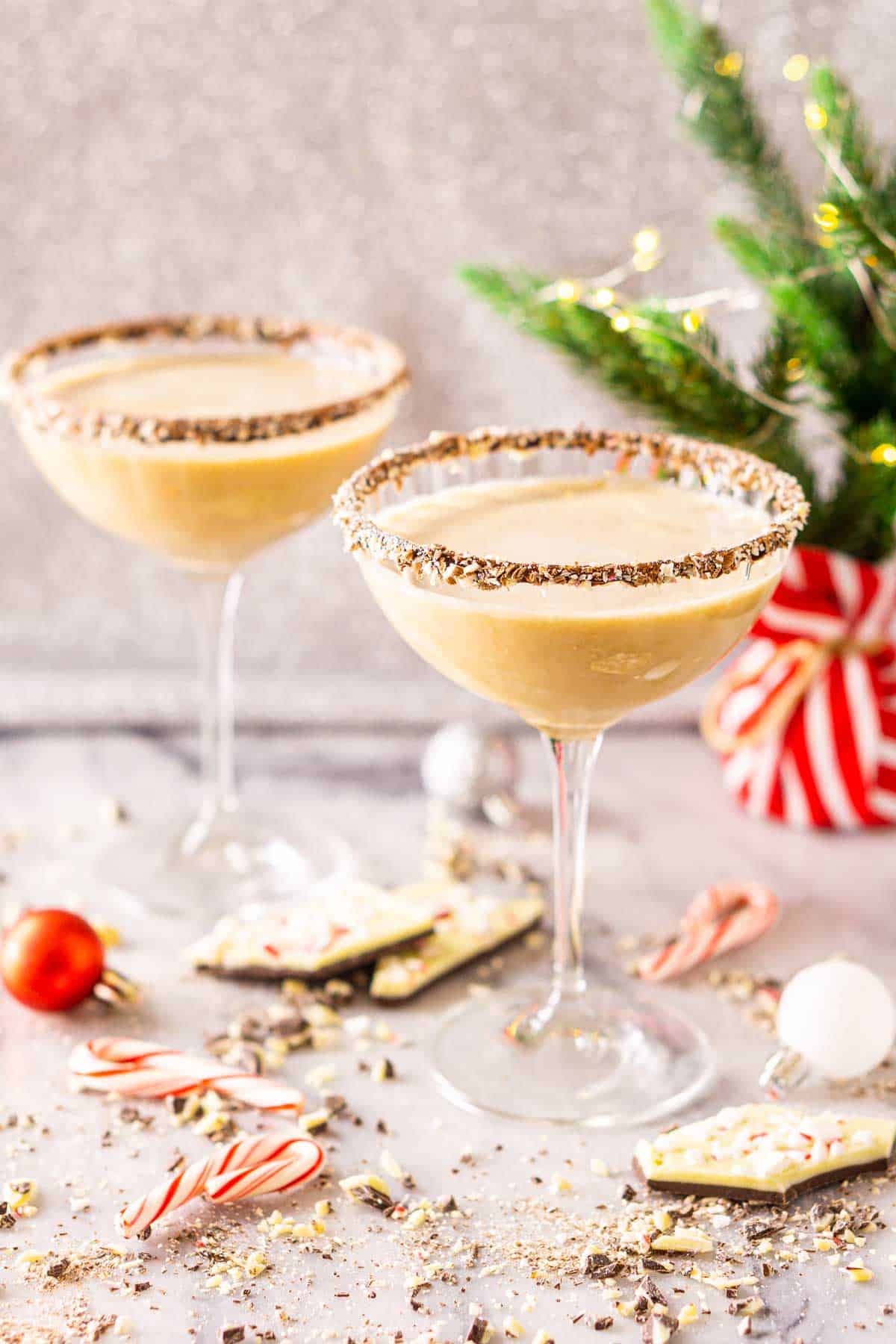 Two peppermint-chocolate martini cocktails on a white marble countertop with ornaments and chocolate around them.