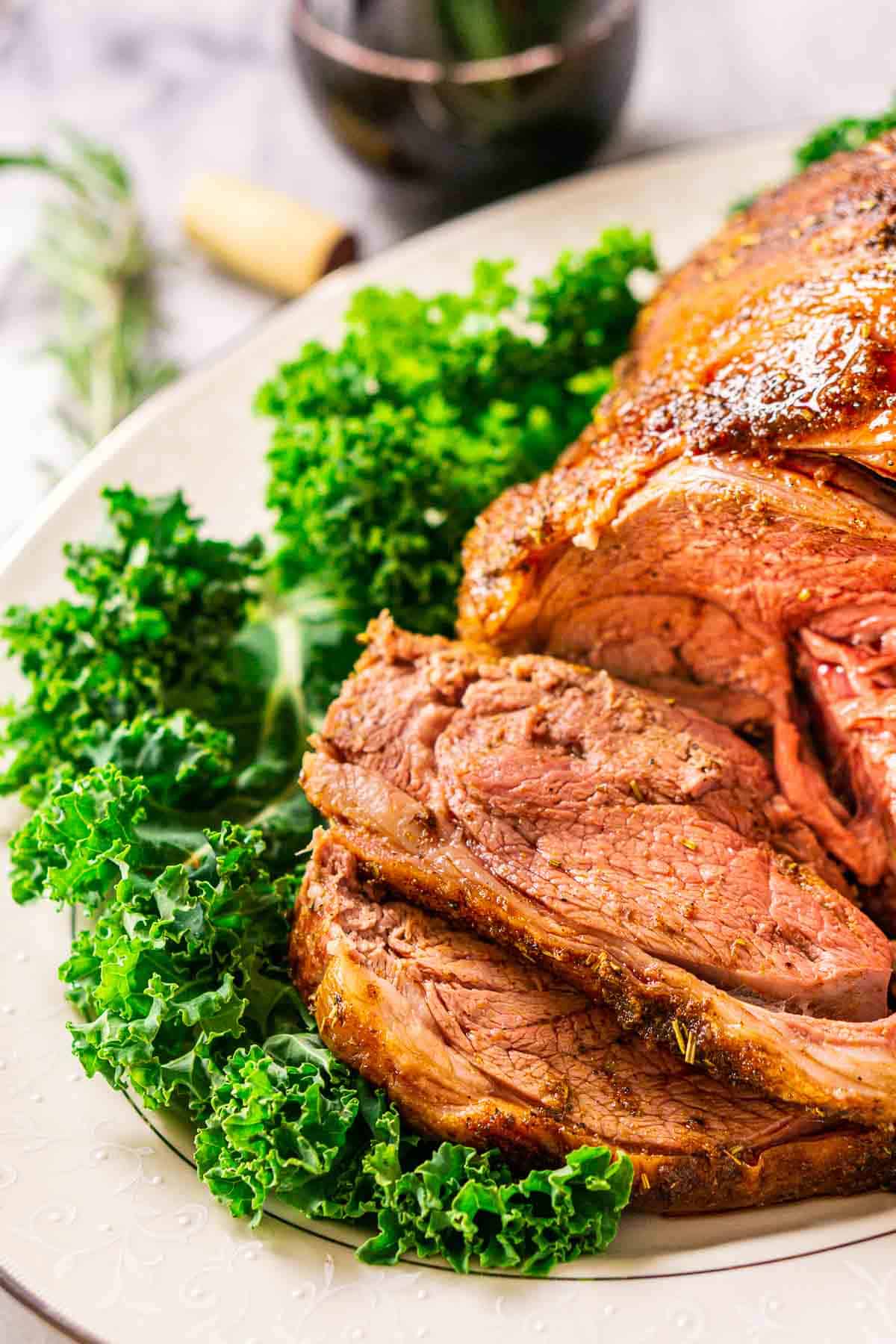 A close-up view of slices of the smoked leg of lamb on a white platter with decorative green lettuce.