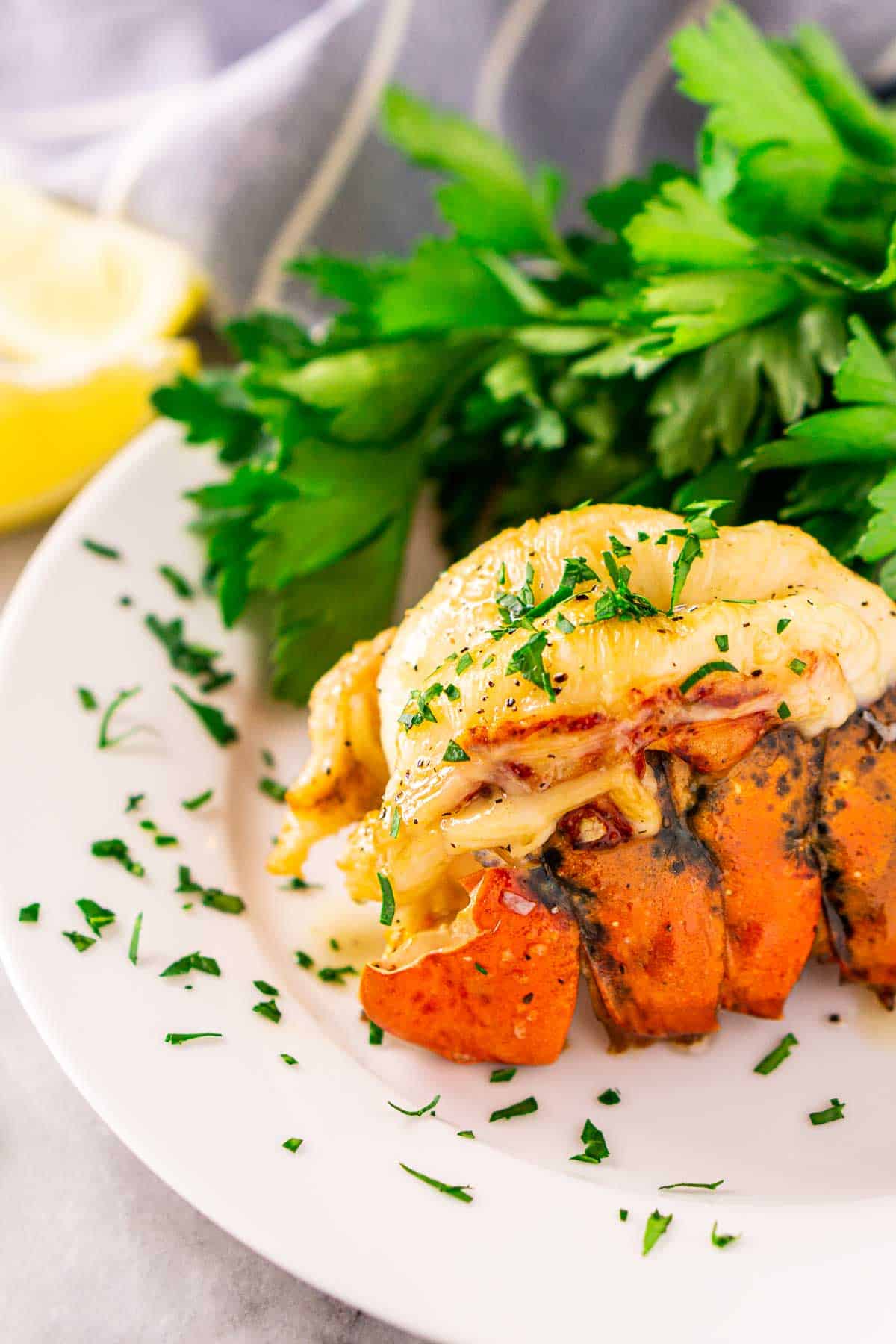 Looking down on one of the smoked lobster tails on a white plate with a bunch of parsley in the background.