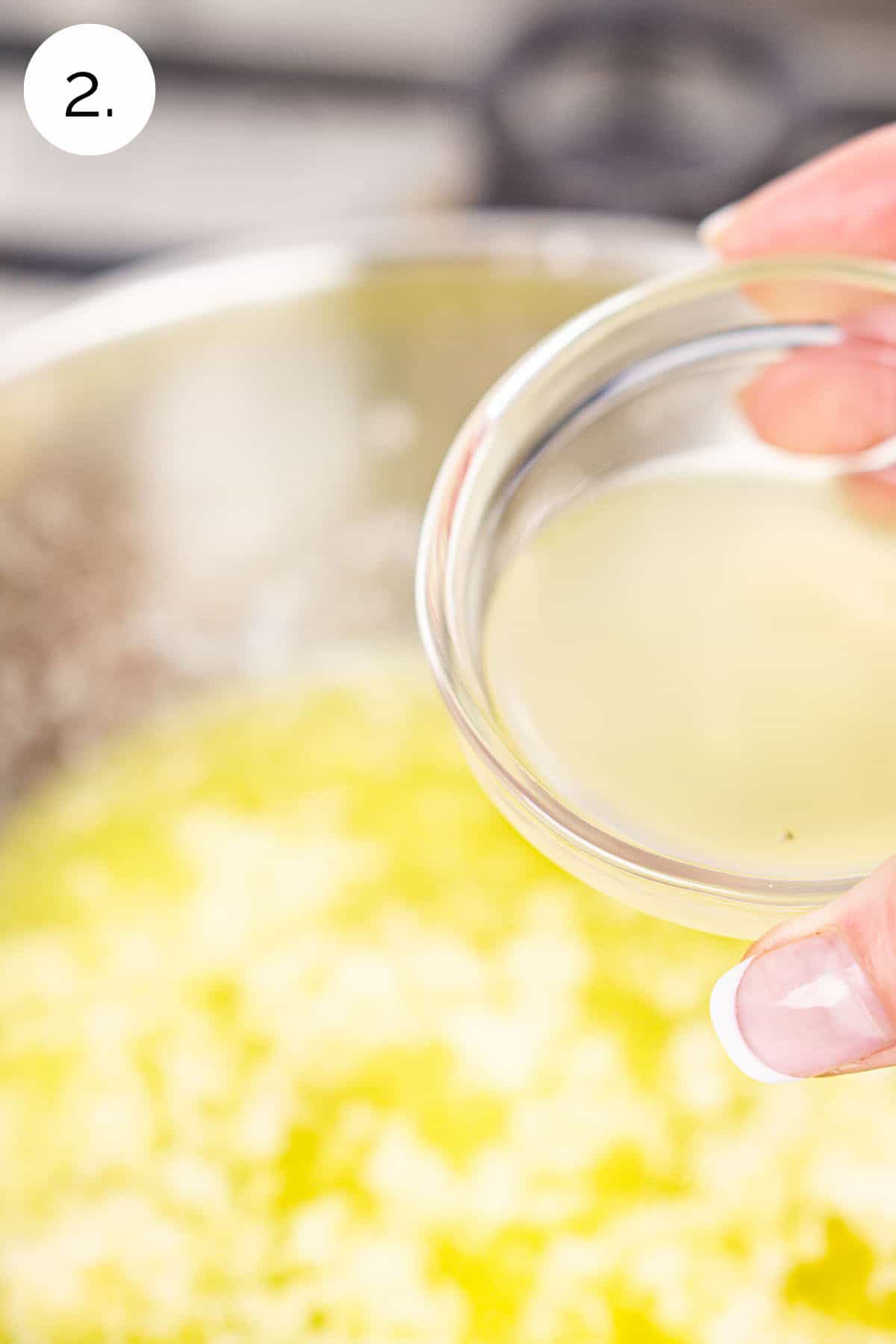 A hand pouring a small bowl of lemon juice into the garlic-butter mixture in a small saucepan.