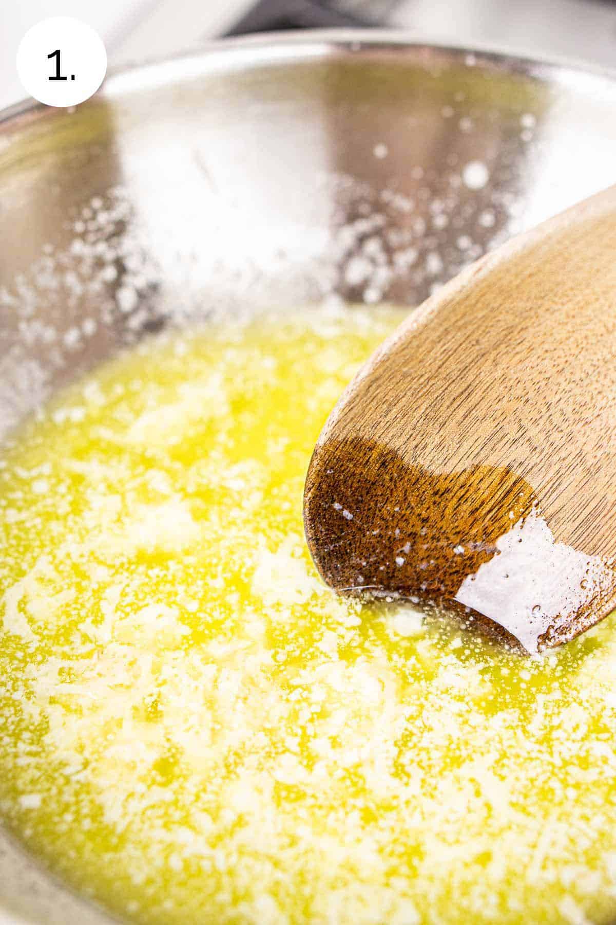 A wooden spoon stirring together the melted butter and garlic in a small stainless saucepan on the stove.
