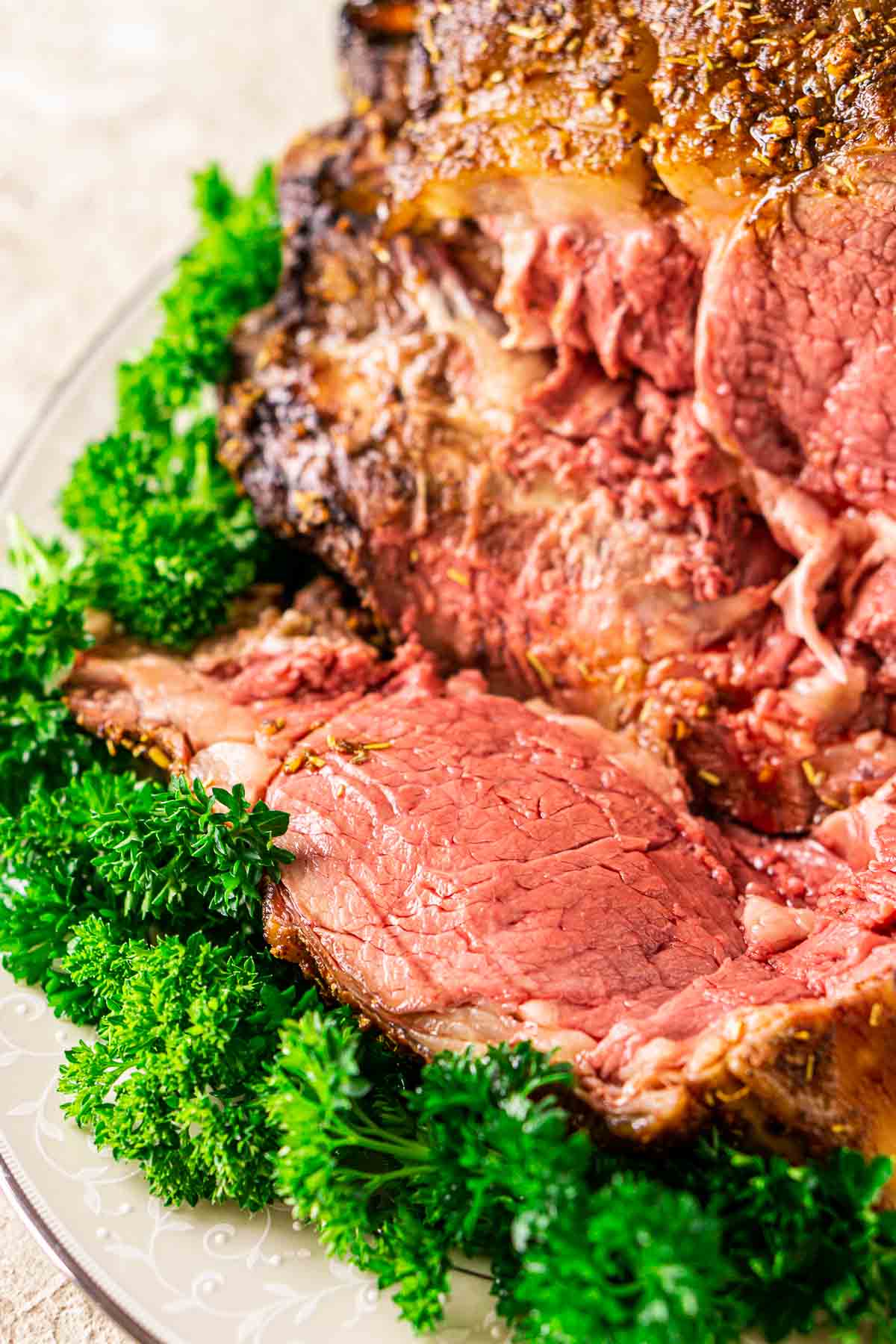 A close-up shot of a slice of the smoked prime rib on a platter with green parsley underneath as a garnish.