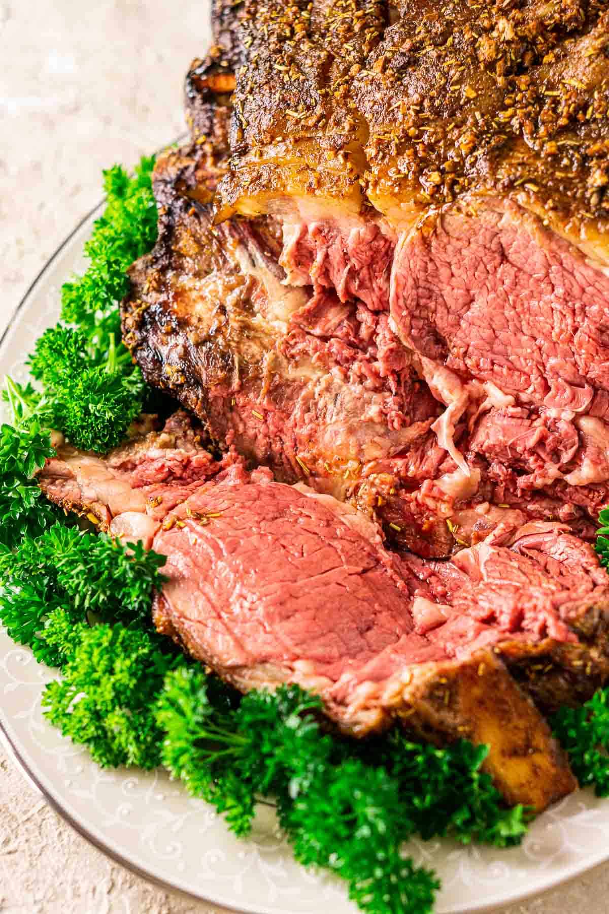Looking down on the smoked prime rib roast on a cream-colored platter with green parsley around it.