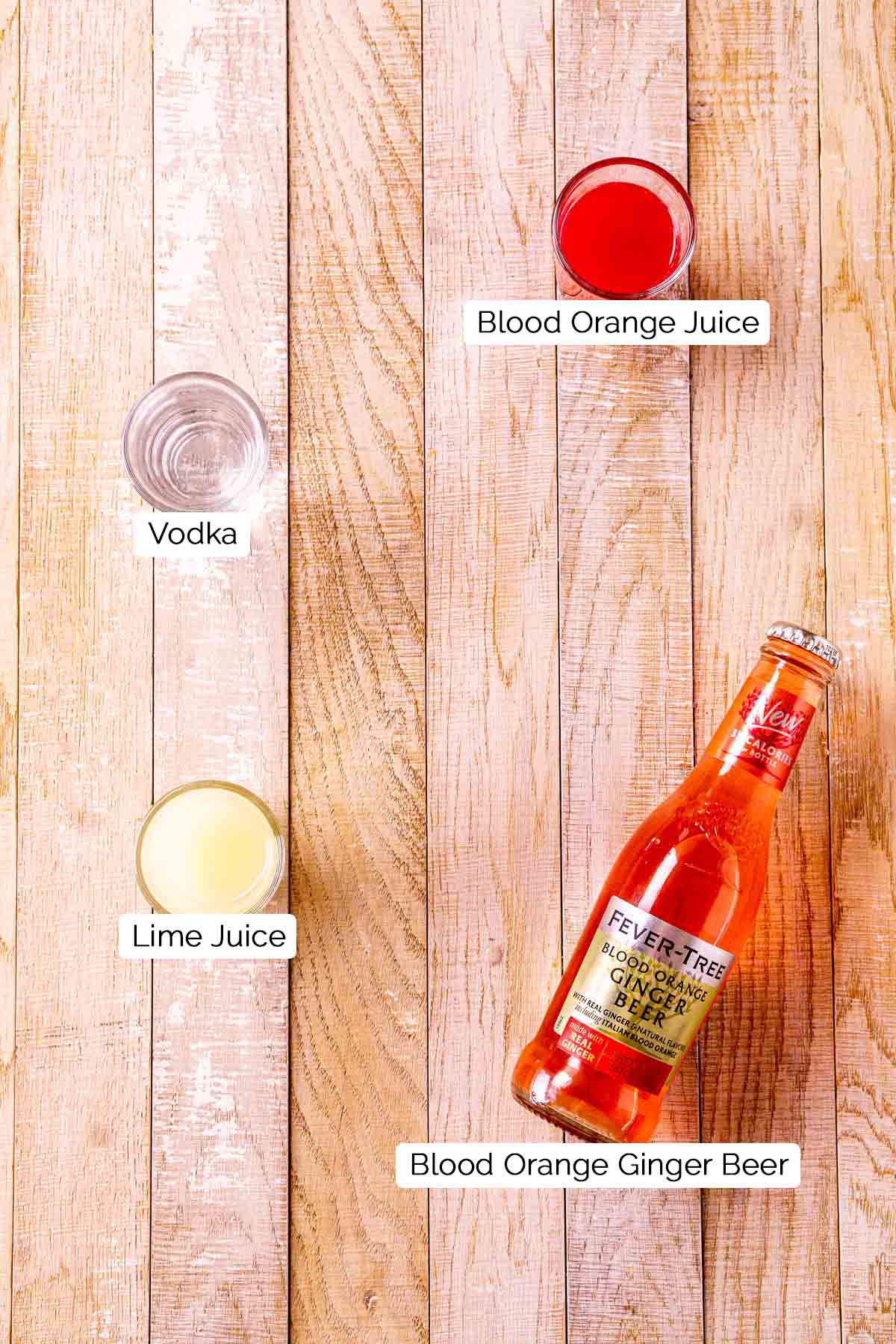 The drink ingredients on a cream-colored wooden surface with black and white labels underneath each item.