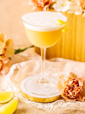 A Boston sour on a white coaster with lemon wedges to the side and pink carnations surrounding it.
