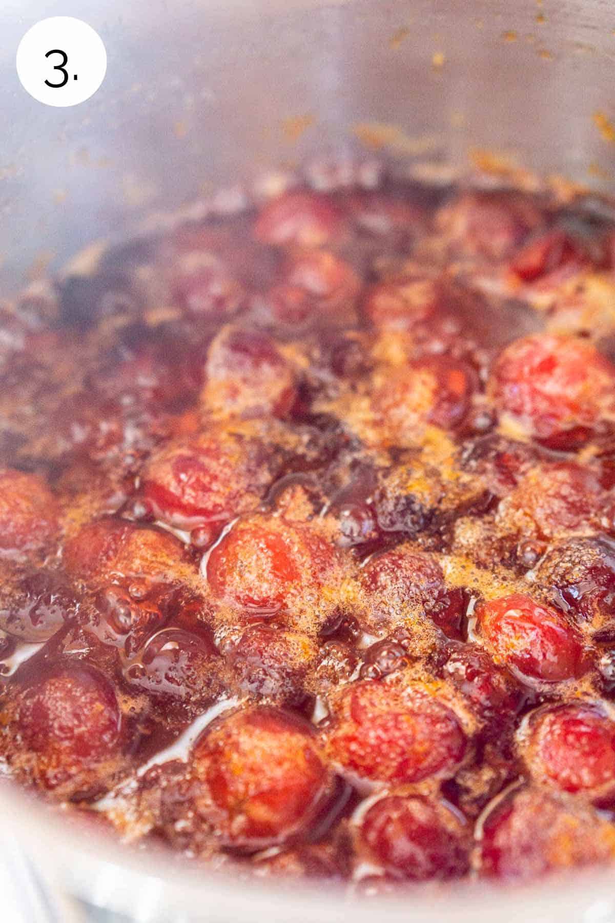 The cranberry syrup simmering on the stove in a small stainless steel saucepan.