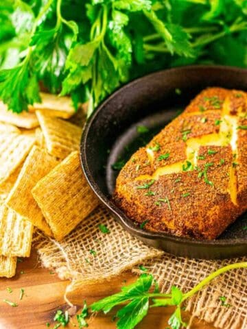 Looking down on a block of smoked cream cheese in a small cast-iron skillet with crackers and a bunch of parsley in the background.