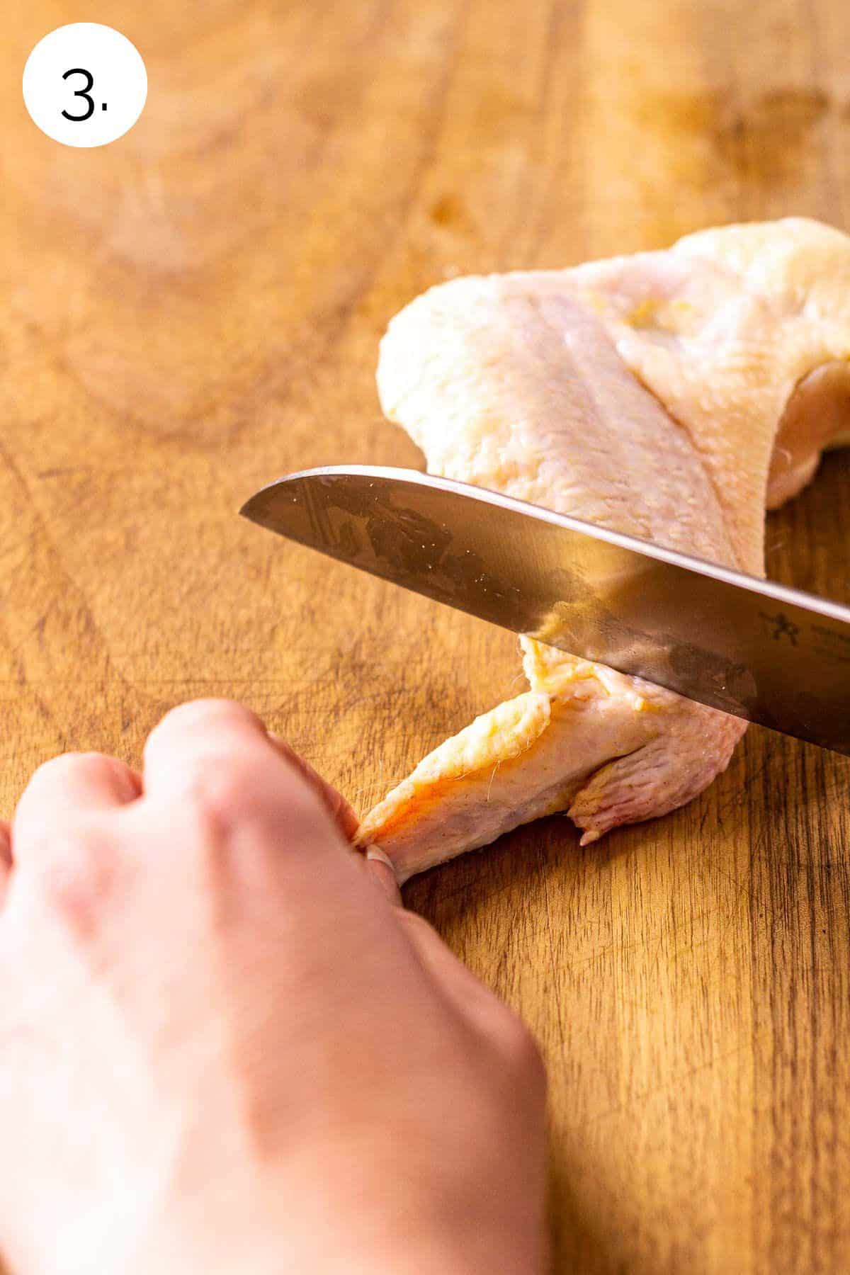 A butcher knife slicing off the wing tip on a brown wooden cutting board.