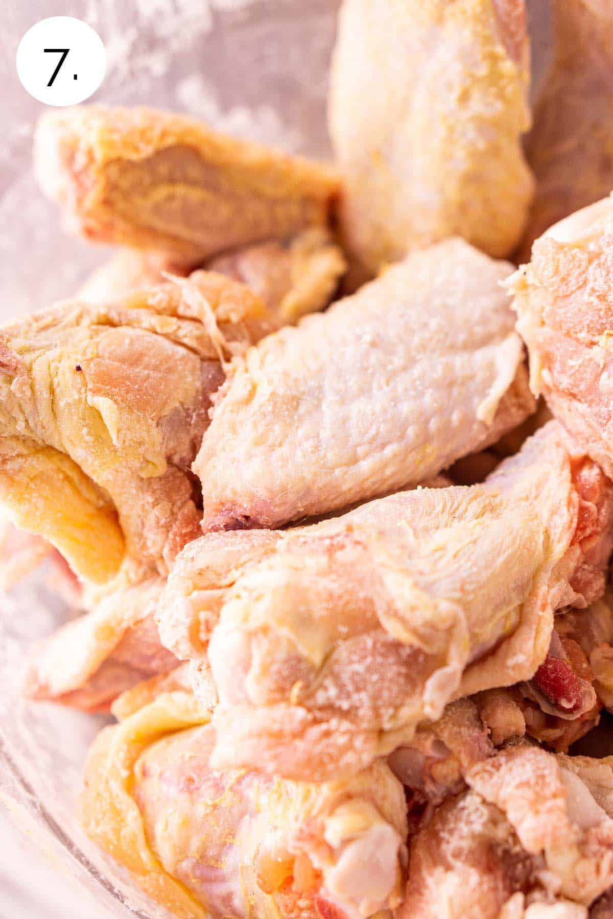 The chicken pieces in a large glass mixing bowl after they've been coated with baking powder.