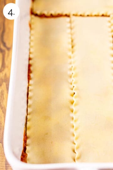 The lasagna noodles layered on top of the tomato sauce in a white baking dish on a brown wooden surface.