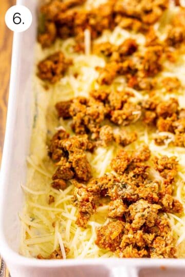 The crumbled meatballs layered on top of the noodles and cheese layer in a white baking dish.
