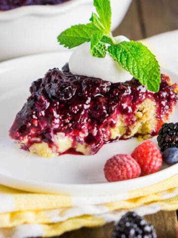 A slice of the mixed berry custard pie on a small plate on top of a yellow and white napkins with fresh berries in front.