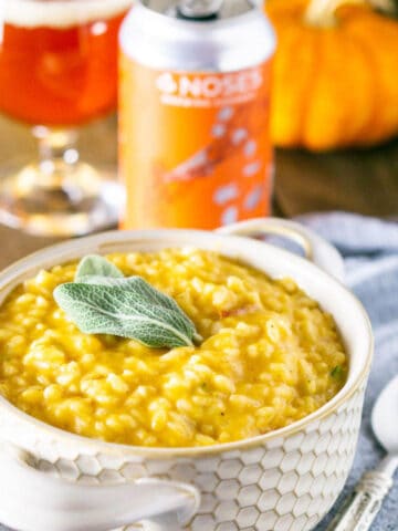 The pumpkin ale risotto in a cream-colored bowl on blue clothe with a pumpkin beer in the background.