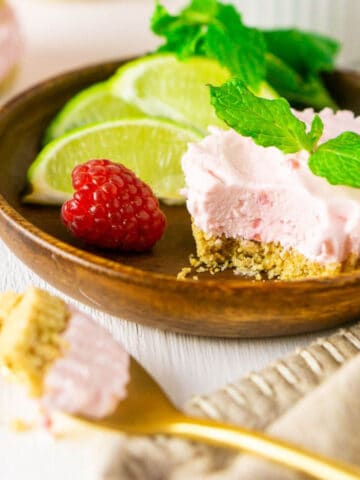 A mini raspberry mojito pie with a scoop taken out of it on a wooden plate with a gold spoon holding some of the pie in front.
