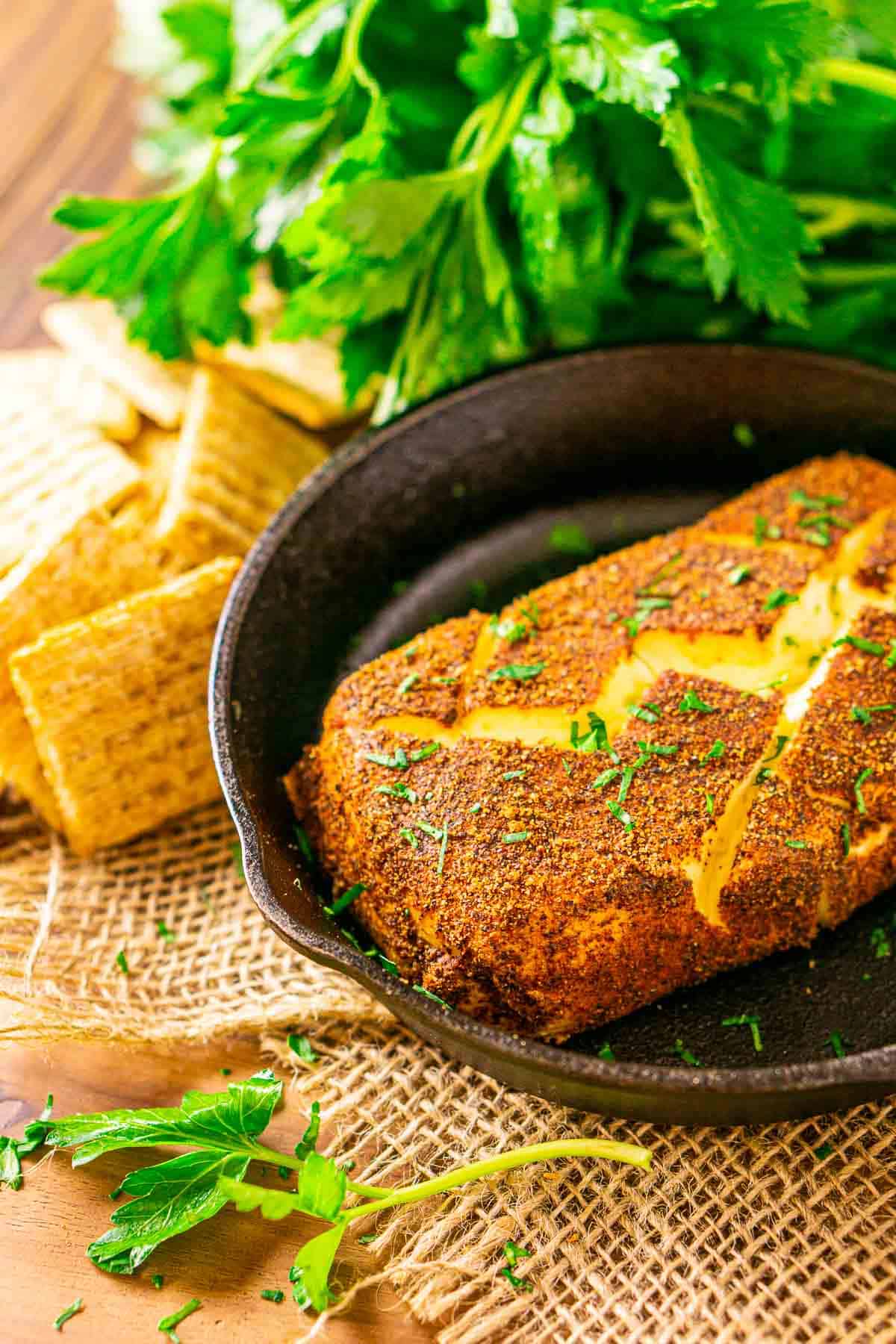 A side view of the smoked cream cheese in a cast-iron skillet on burlap with a sprig of parsley in front.