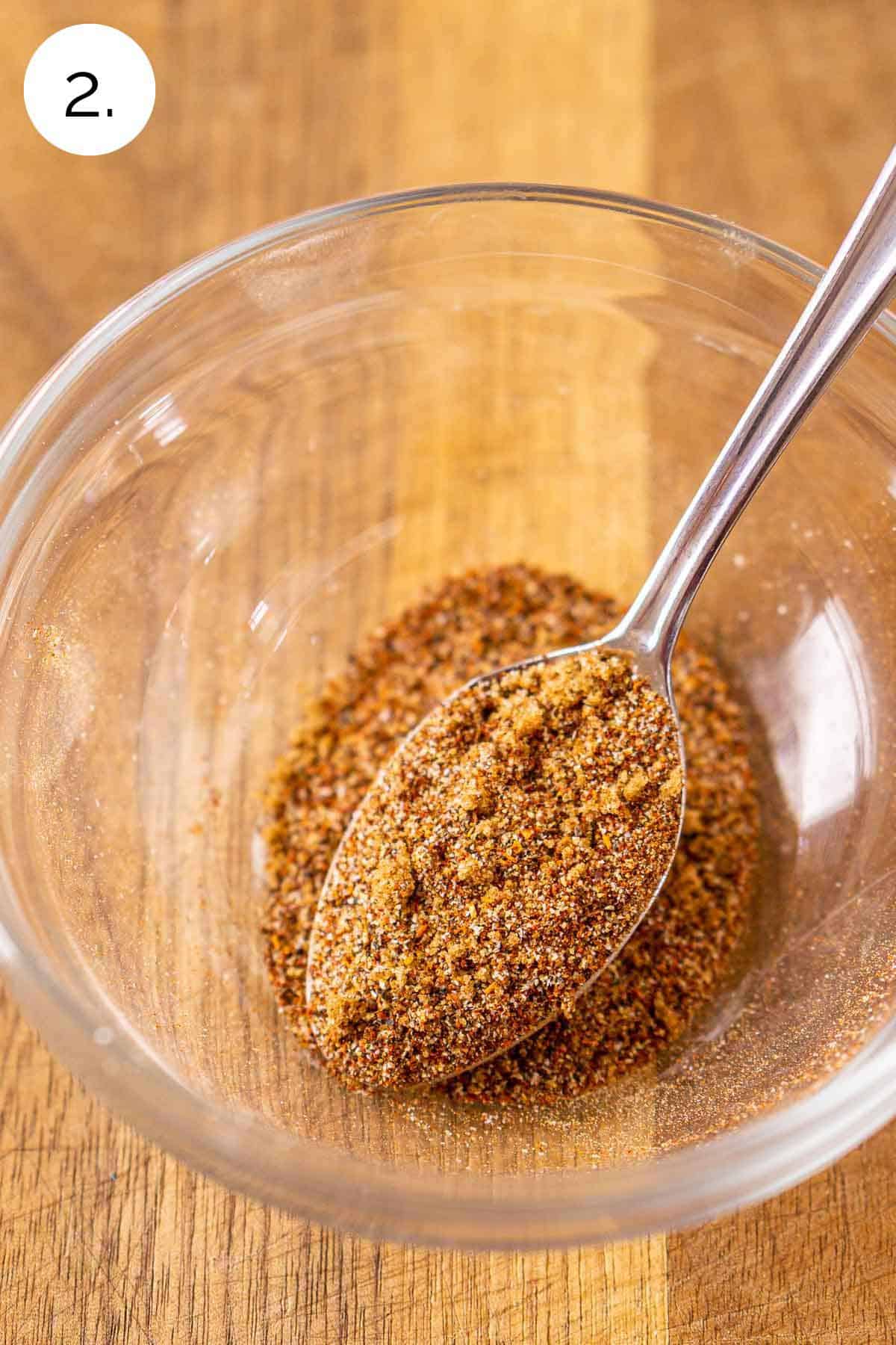 A spoon in a small glass bowl showing the dry rub after it's been stirred together to make one cohesive mixture.