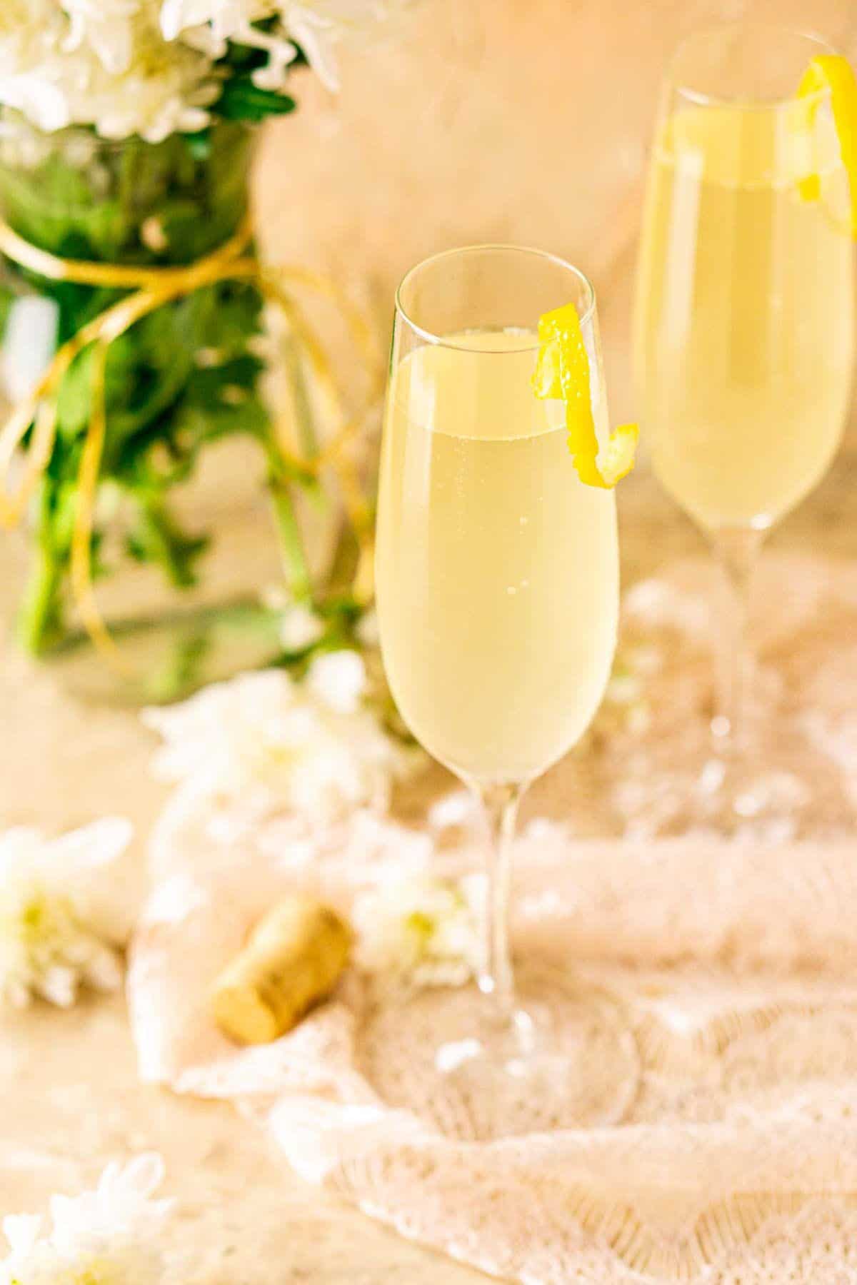 A French 76 on cream-colored lace with white flowers around it and a bouquet in the background.