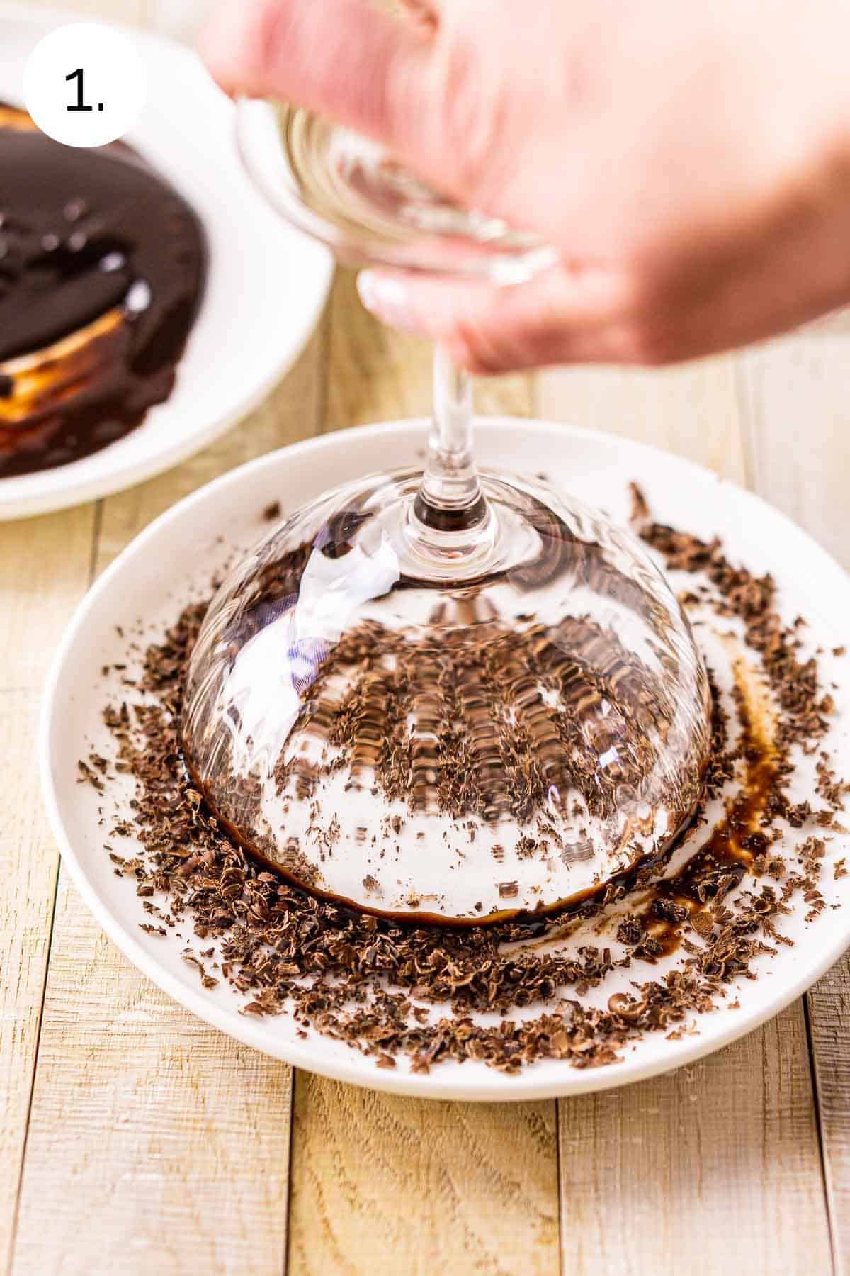 A hand dipping the rim of the martini glass into a small white plate of grated chocolate.