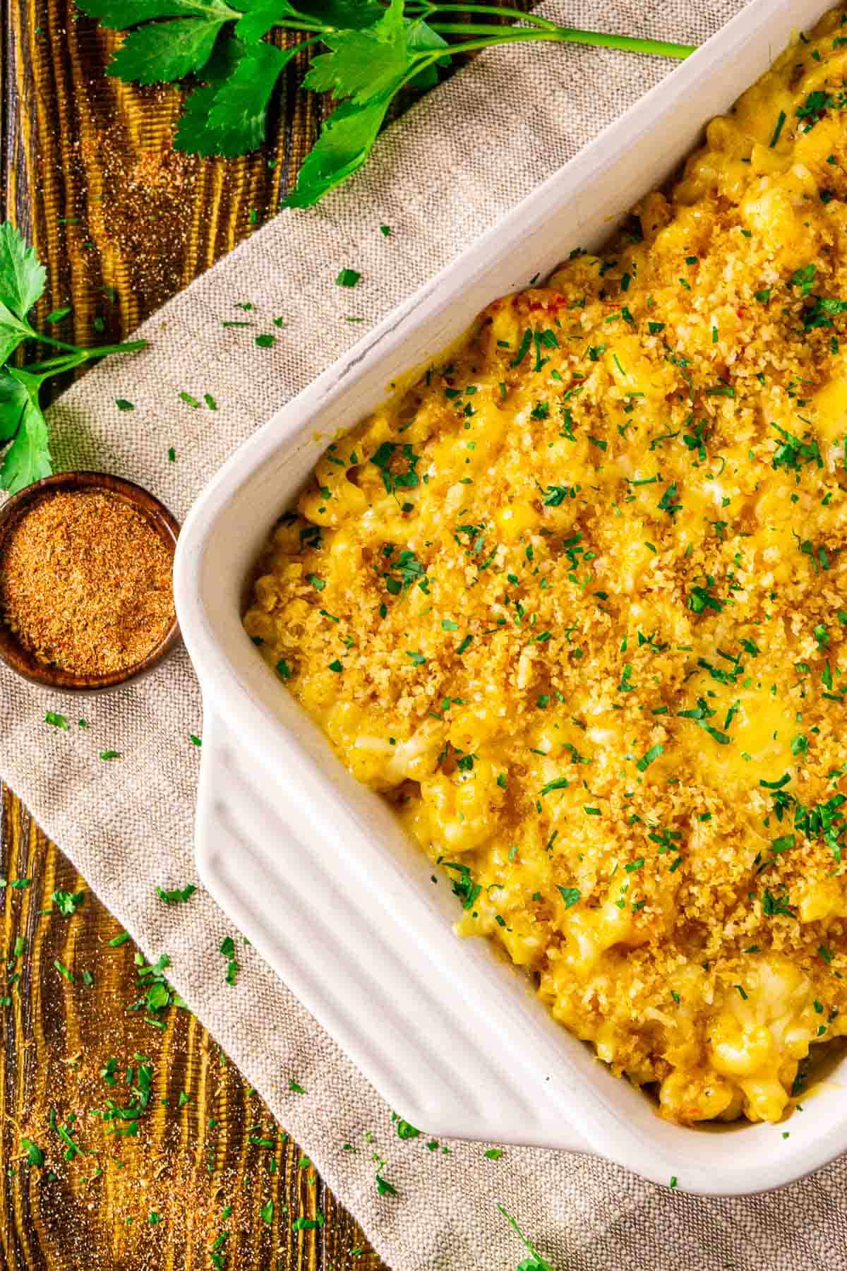 An aerial view of the crawfish mac and cheese in a white baking dish with Cajun seasoning and parsley scattered around it.