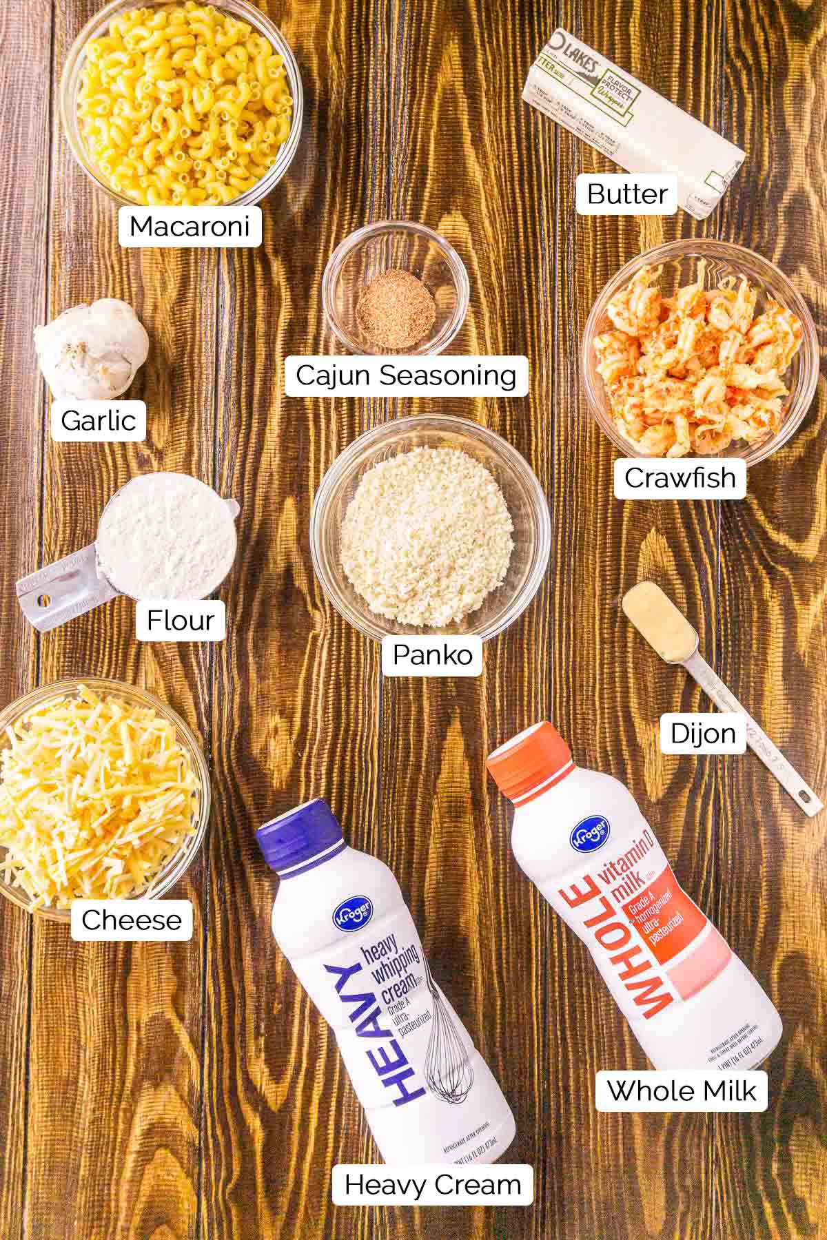 The mac and cheese ingredients on a wooden surface with black and white labels underneath each item.
