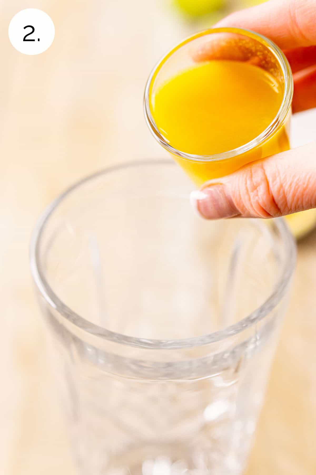 A hand pouring a shot glass filled with passion fruit purée into a crystal cocktail shaker to start mixing the drink.