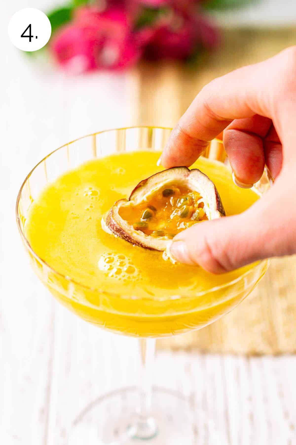 A hand placing a slice of fresh passion fruit on top of the drink to float in the martini glass.