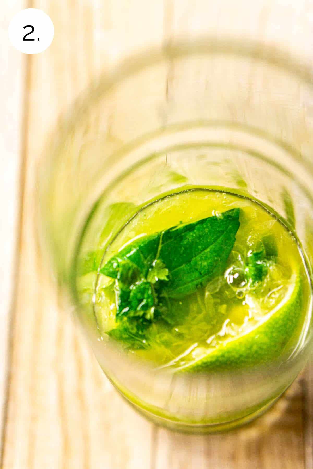 The drink on a cream-colored board with the mint on top of the lime wedge after it's been lightly muddled.