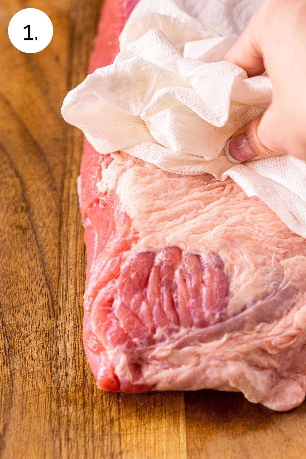 A hand blotting the corned beef dry with a paper towel on a brown cutting board after rinsing in cold water.