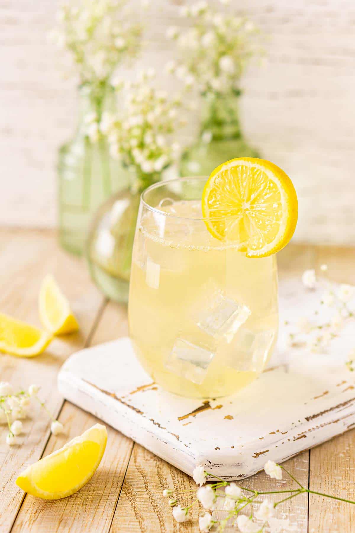 A side view of the St. Germain elderflower spritz on a white serving tray with flowers and lemon slices to the left.