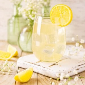 A straight-on view of the St. Germain elderflower spritz on a white wooden tray with white flowers in the background and lemon slices to the side.