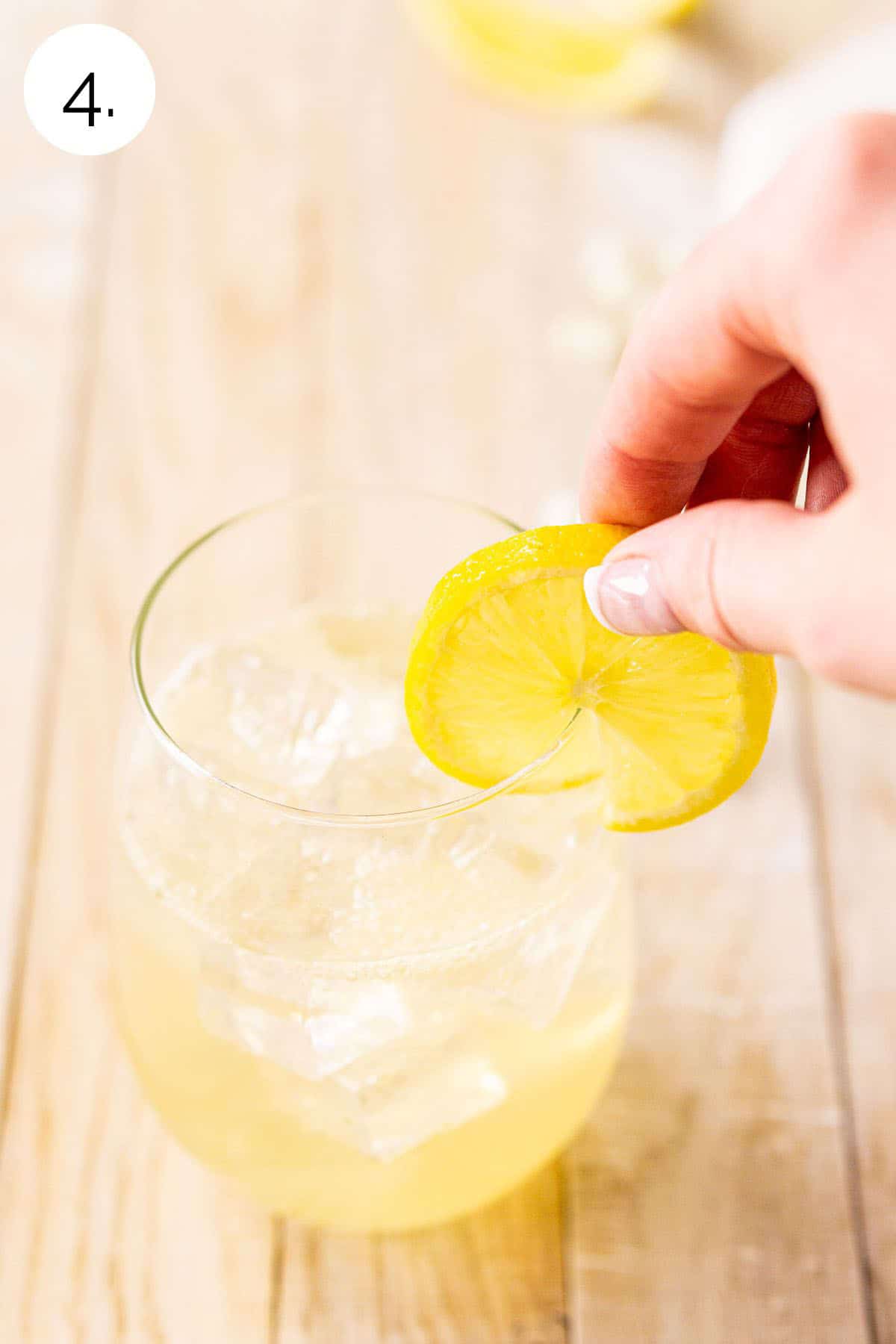 A hand placing a lemon wheel on the rim of the wine glass to garnish for a finishing touch.